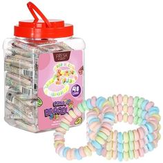 a jar filled with lots of candy next to a bunch of bracelets on a white background