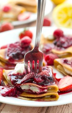 a fork sticking into some pancakes with fruit on top