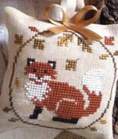 a cross stitch pillow with a red fox on it's side and a ribbon tied around the edge