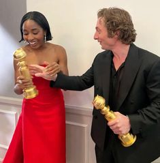 a woman in a red dress and a man in a black suit holding two oscars