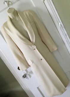 Ivory colored 2-button front 1990's vintage 3/4 length blazer/jacket, made in Franc, is by LOUIS FERAUD. This blazer/jacket is a 3/4 length, hitting mid-calf, is lined in silk, which has the 'Louis Feraud' name embossed all over the silk fabric (photo 6). The outer or shell fabric is a textured worsted wool (photo 7) Long shawl lapel, 2 goldtone buttons at the front placket for closure. Welt pocket at the right breast and 2 flap pockets at the right and left hip area. Long barrel sleeves, princess seams in the front and side back. The back has a decorative buttoned martingale band (photo 5). Coloring is a creamy ivory...like a vanilla. This long jacket/blazer was made in the 1990's in FRANCE. Size tag is missing; I estimated the size based on the measurements, to be a size 4. There's a tin Cream Lapel Collar Blazer With Single Button, Cream Blazer With Single Button And Lapel Collar, Cream Single Button Blazer With Lapel Collar, Cream Notch Lapel Outerwear With Single Button, Classic Cream Single-breasted Blazer, Cream Outerwear With Double Button And Notch Lapel, Cream Outerwear With Single Button And Lapel Collar, Cream Blazer With Button Closure And Lapel Collar, Cream Single Button Outerwear For Work