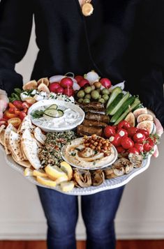 a woman is holding a platter full of different types of appetizers and dips