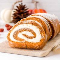 a cinnamon roll with cream cheese frosting on a cutting board next to pumpkins and pine cones