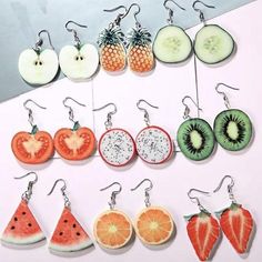 fruit earrings are hanging from hooks on a white surface with an advertisement in the background