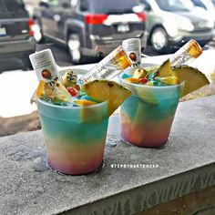 two cups filled with ice cream and fruit on top of a cement ledge next to parked cars