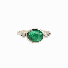 This elegant ring features a captivating 1.72 carat oval-shaped east west emerald, set in a polished band. Flanking the central stone are two round natural earth mined diamonds, adding a touch of sparkle. The emerald's rich green color is beautifully complemented by the warm tone of the band, creating a harmonious and refined look. The design is understated yet sophisticated, focusing on the natural beauty of the gemstones. This ring is made with solid 14K Gold and natural Earth mined SI / G-H d Solitaire Studs, Jewelry Appraisal, East West, Natural Earth, Elegant Ring, Custom Jewelry Design, Emerald Ring, Emerald, Fine Jewelry