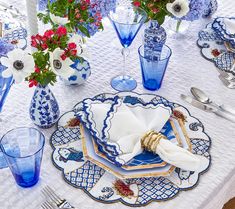 a table set with blue and white plates, silverware and flowers in vases