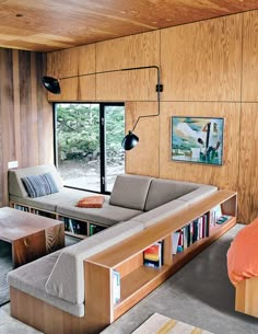 a living room filled with furniture next to a large window and a wooden paneled wall