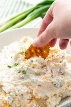 a hand dipping a cracker into a bowl of potato salad