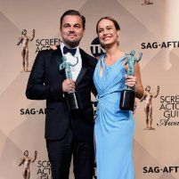 two people standing next to each other holding awards