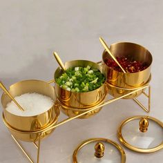 three brass bowls with chopsticks and vegetables in them sitting on a white surface