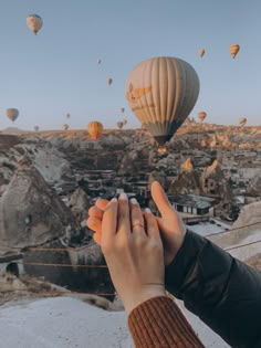 a person holding their hand up to the sky with hot air balloons in the background