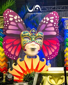 a colorful butterfly mask sitting on top of a table next to a vase and clock