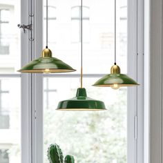 two green lights hanging over a window next to a potted cactus in a vase