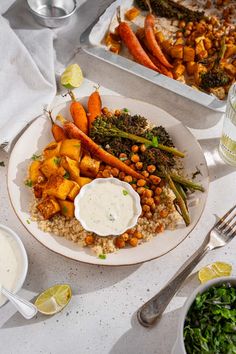 a white plate topped with lots of veggies and rice next to bowls of dipping sauce