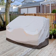 a car covered in a white cover sitting on top of a wooden deck next to a tree