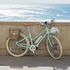 a bicycle leaning against a wall next to the ocean with a basket on it's handlebars