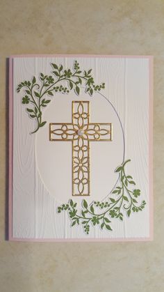 a card with a cross on the front and green leaves around it, sitting on top of a table