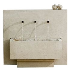 a concrete fountain with three faucets and two rocks on the ground next to it