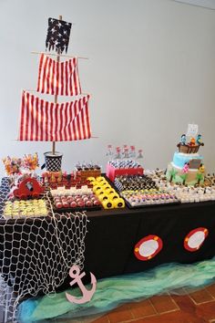 a table topped with lots of cakes and cupcakes next to a pirate ship