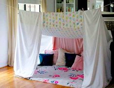 a white canopy bed with pink and blue pillows on top of it in a room