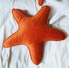 an orange starfish pillow sitting on top of a white bed sheet next to two pillows