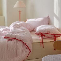 an unmade bed with pink and white striped comforter, pillows and lamps on either side