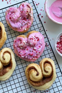 four doughnuts with pink frosting and sprinkles on a cooling rack