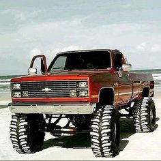 a red truck with big tires parked on the beach