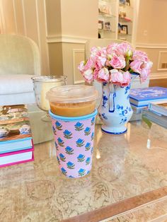 a table topped with a vase filled with pink flowers next to a cup of coffee