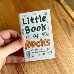 the little book of rocks is being held by someone's hand on a wooden table