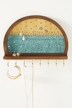 a wooden shelf with jewelry hanging from it's sides and a clock on the top