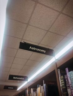 a sign that reads astronomy hangs from the ceiling in a library with bookshelves