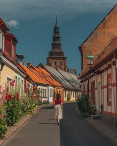 a woman is walking down the street in front of some old buildings with red flowers