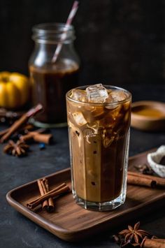 an iced drink in a glass on a tray with cinnamon sticks and spices around it