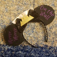 a mickey mouse ears with the word on the wall written in purple and gold glitter