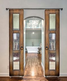 an open door leading to a bathroom with a tub and chandelier in the background