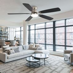 a living room with couches, chairs and a ceiling fan in front of large windows