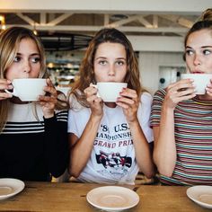 three women sitting at a table drinking from mugs with their hands in front of them