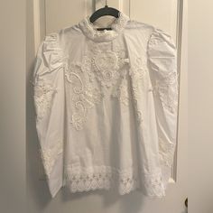 White Cotton Top. Back Neck Tied With Single Button. Standing Collar With Lace Detail. Lace Hem. Embroidered Front And Sleeve. Elegant Cotton Eyelet Tops, Cotton Eyelet Puff Sleeve Tops, Cotton Eyelet Long Sleeve Tops, Cotton Eyelet Tops With Puff Sleeves, White Puff Sleeve Top With Floral Embroidery, Chic White Embroidered Top With Lace Trim, Feminine Embroidered White Tops, Cotton Embroidered Long Sleeve Top With Lace Trim, Elegant Cotton Embroidered Top With Broderie Anglaise