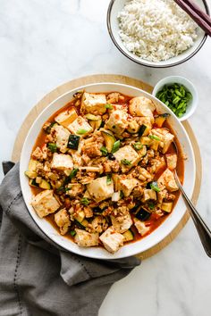 a white bowl filled with tofu and rice next to two bowls of green vegetables