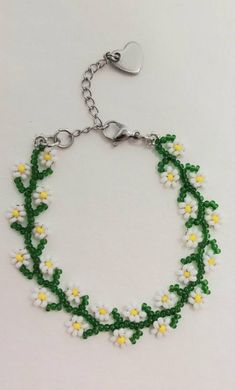 a green and white beaded bracelet with daisies attached to it on a silver chain