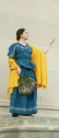 a woman in blue and yellow dress standing on steps with her hand out to the side