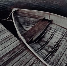 an old wooden boat tied up to a dock with water in the backgroud