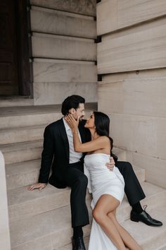 a man and woman are sitting on the steps in front of a building, kissing