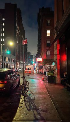 a city street at night with cars and bicycles parked on the side of the road