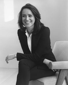 black and white photograph of a woman sitting on a chair with her arms crossed, smiling at the camera