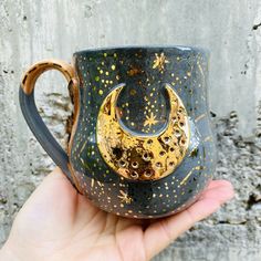 a hand holding a black and gold coffee cup with a crescent design on the side