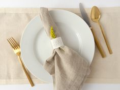 a white plate topped with a yellow flower next to a napkin and silverware on top of a table