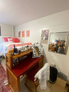 a room with a desk, mirror and pictures on the wall next to a bed